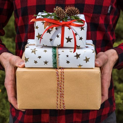 A man wearing a red plaid shirt holding three wrapped gifts