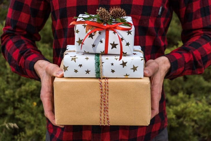 A man wearing a red plaid shirt holding three wrapped gifts