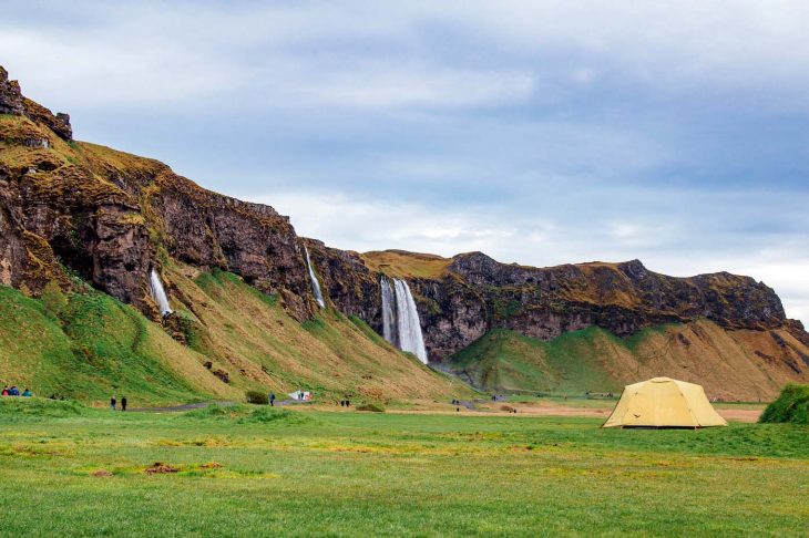 A yellow tent in a field with the Seljalandsfoss waterfall in the backgroundthe