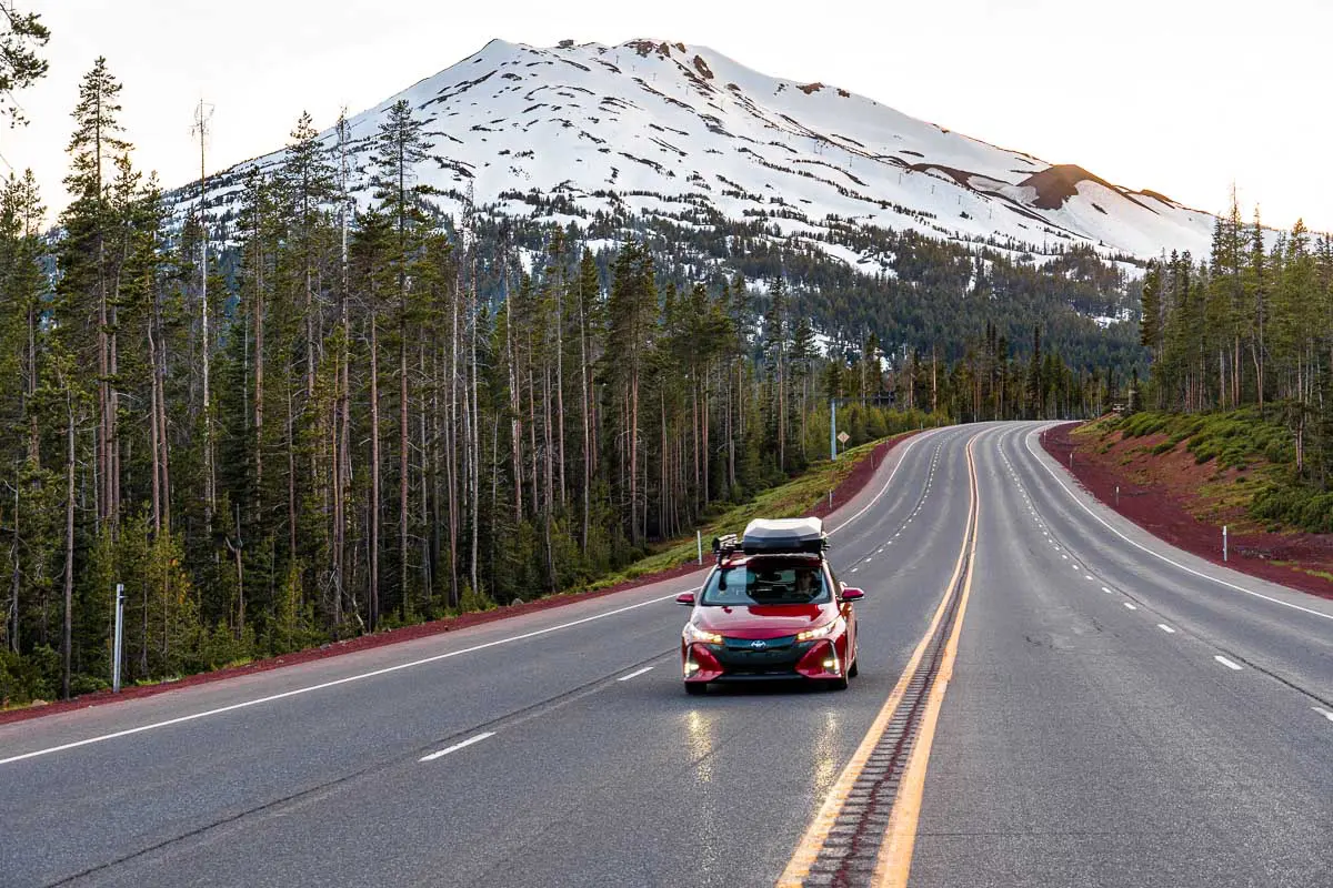 A red Prius Prime driving down a road with a snowcapped mountain in the distance.