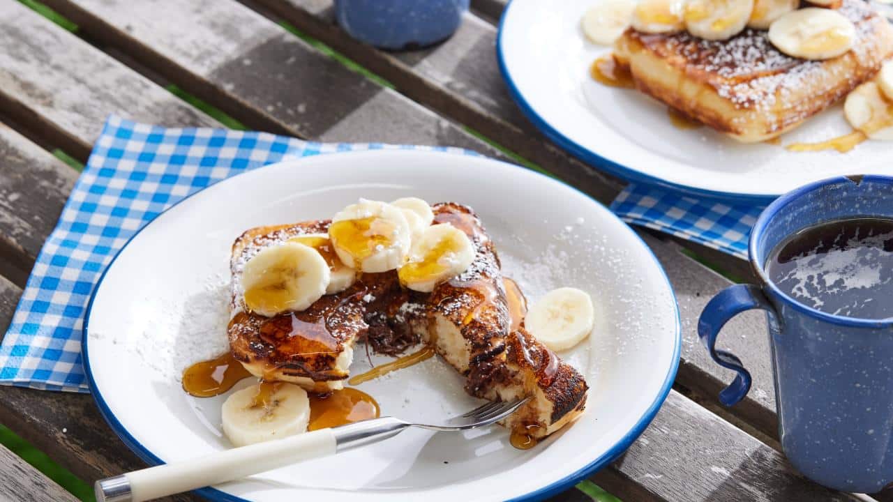 Square pancakes topped with banana slices on a camping plate.
