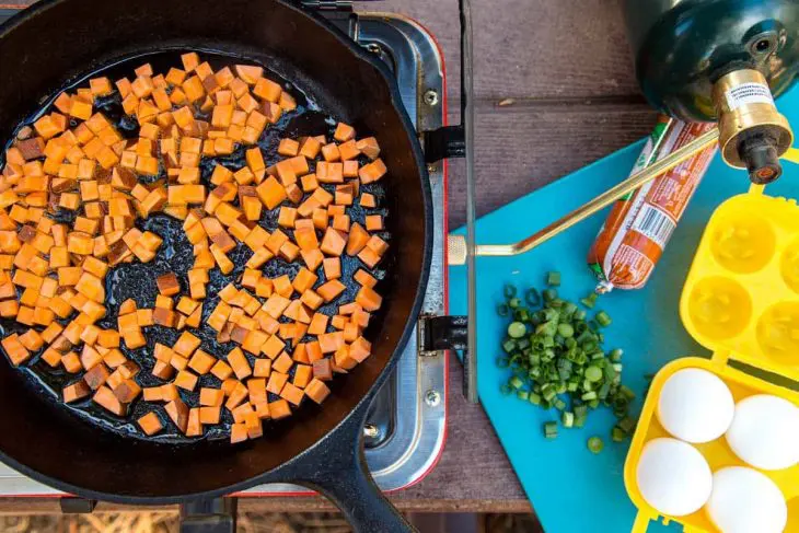 Sweet potatoes in a cast iron skillet with other ingredients to the side.
