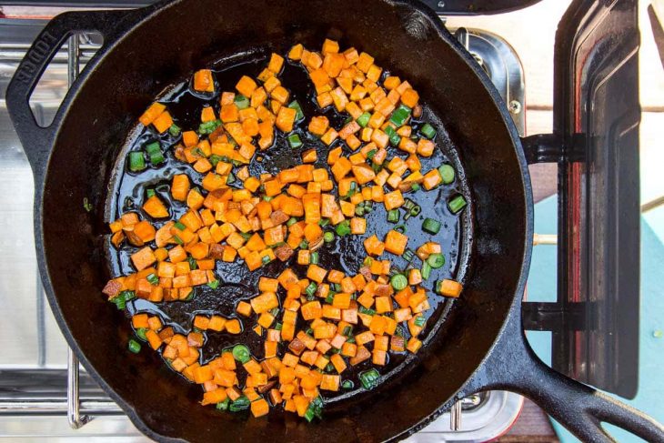 Sweet potatoes and green onions frying in a cast iron skillet