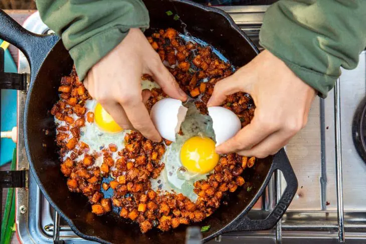Megan cracking an egg into a skillet of sweet potato breakfast hash