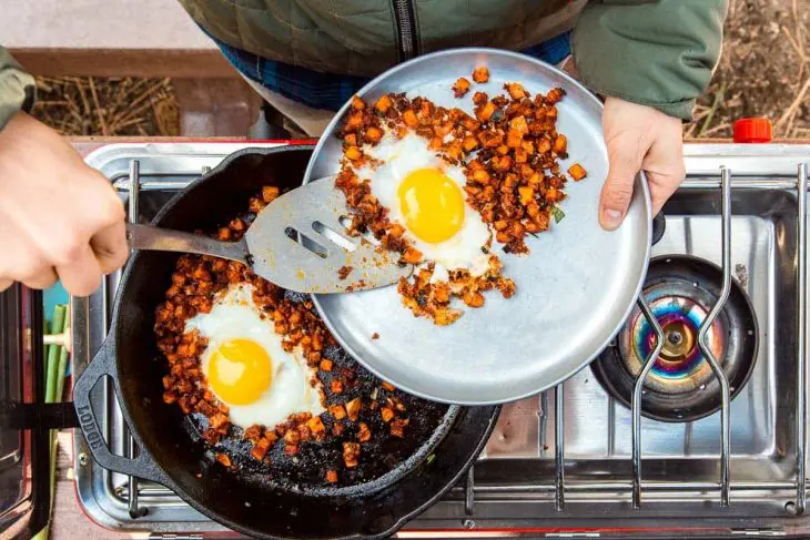 Megan serving an egg and sweet potato hash onto a silver plate.