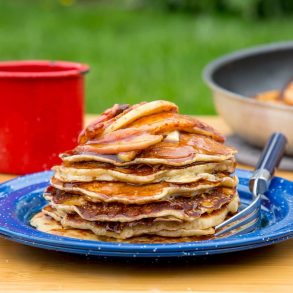 A stack of pancakes with cinnamon apple topping on a blue camping plate.