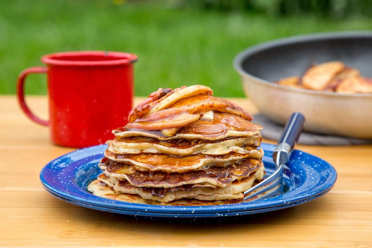 A stack of pancakes with cinnamon apple topping on a blue camping plate.