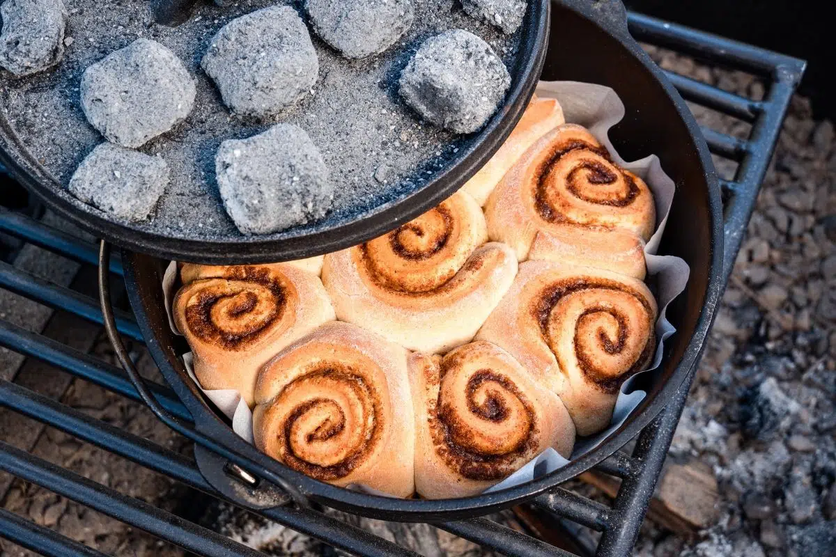 Lifting the lid off a dutch oven to reveal cinnamon rolls