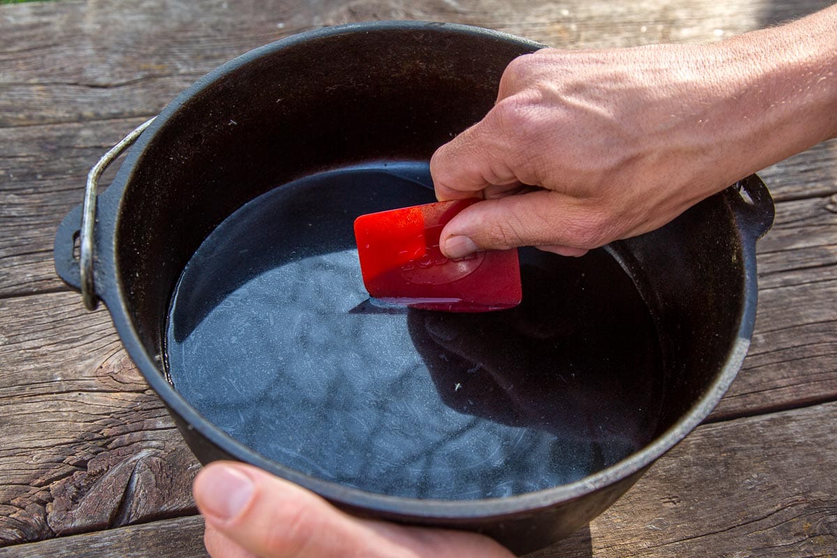 Michael using a red pot scraper to clean a dutch oven filled with water