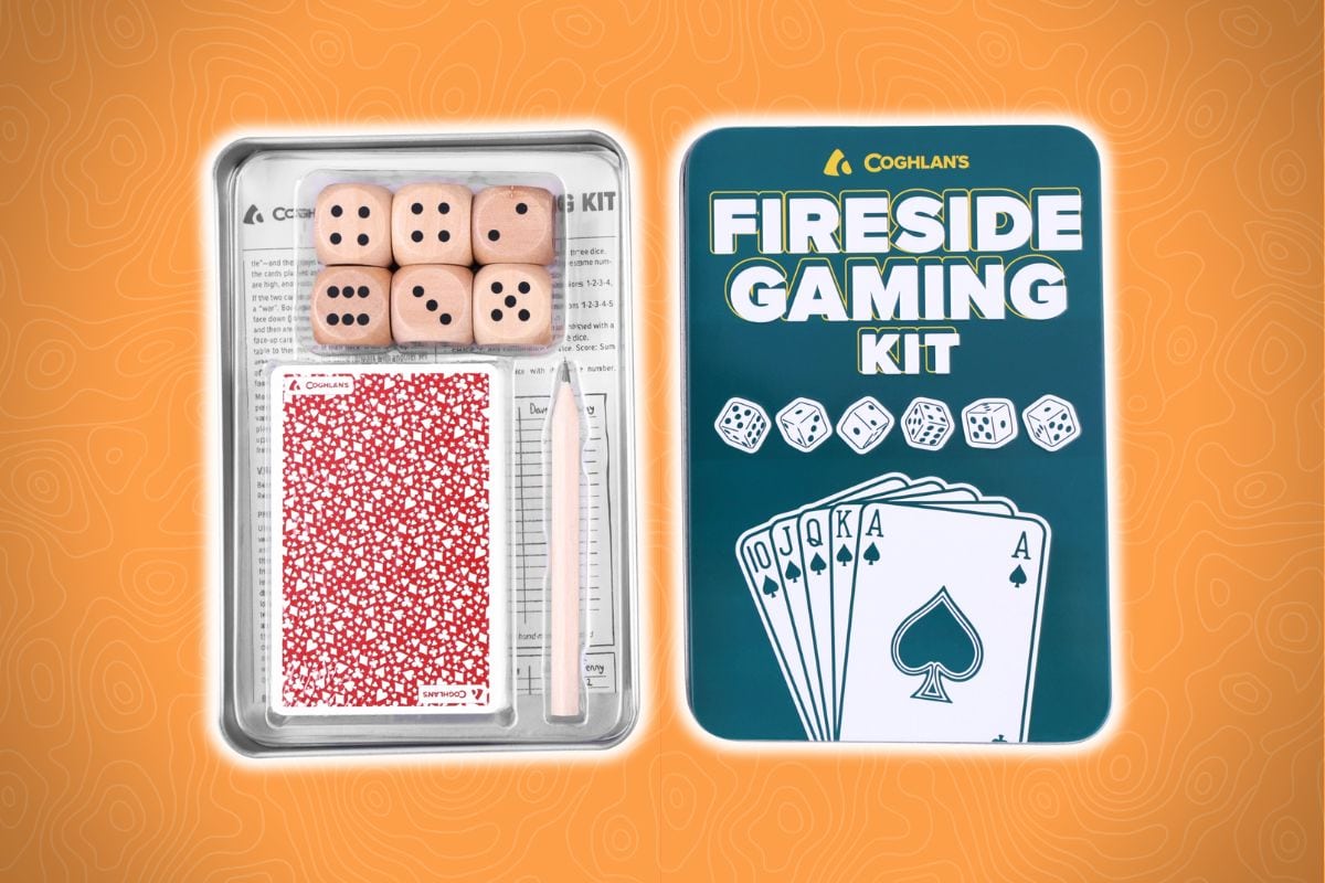 Coghlan’s Fireside Gaming Kit on an orange background with a tin, playing cards, five wooden dice, notepad, and pencil.
