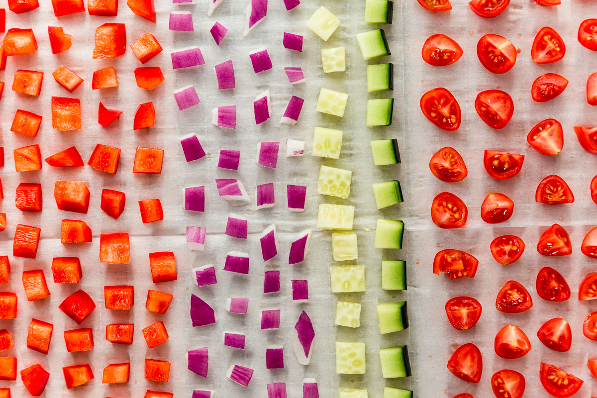 Assorted vegetables cut into small pieces and arranged in rows on a dehydrator tray