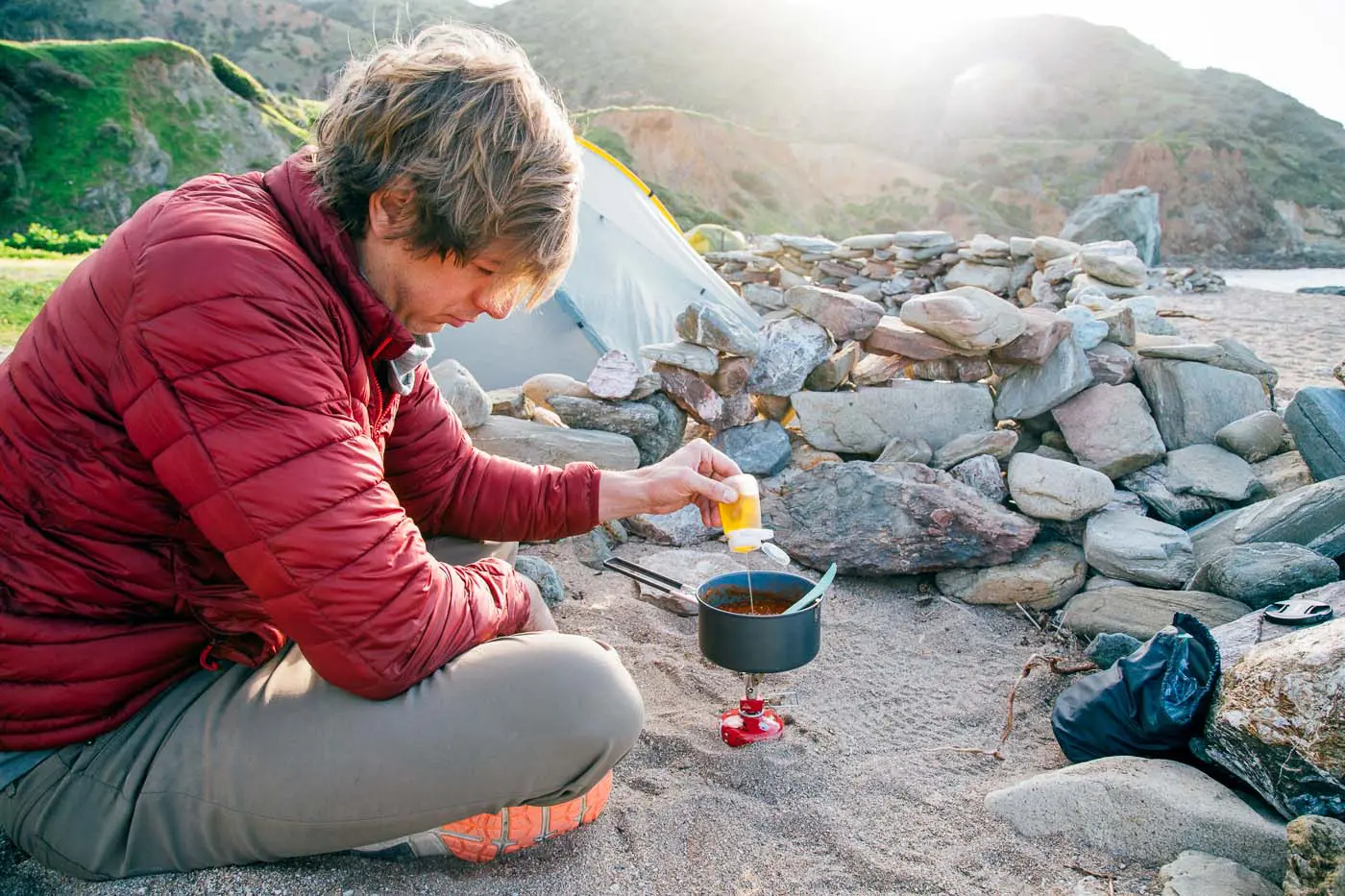 A man adding oil to a backpacking pot full of chili.