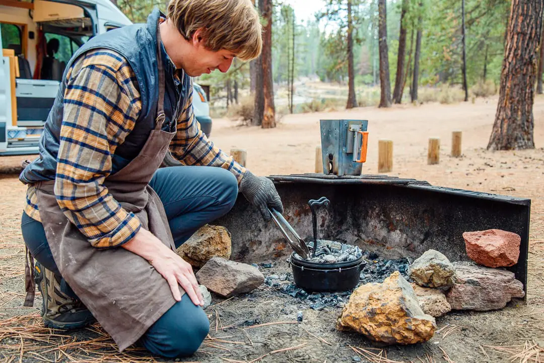 Michael using tongs to place charcoals on top of a camping dutch oven