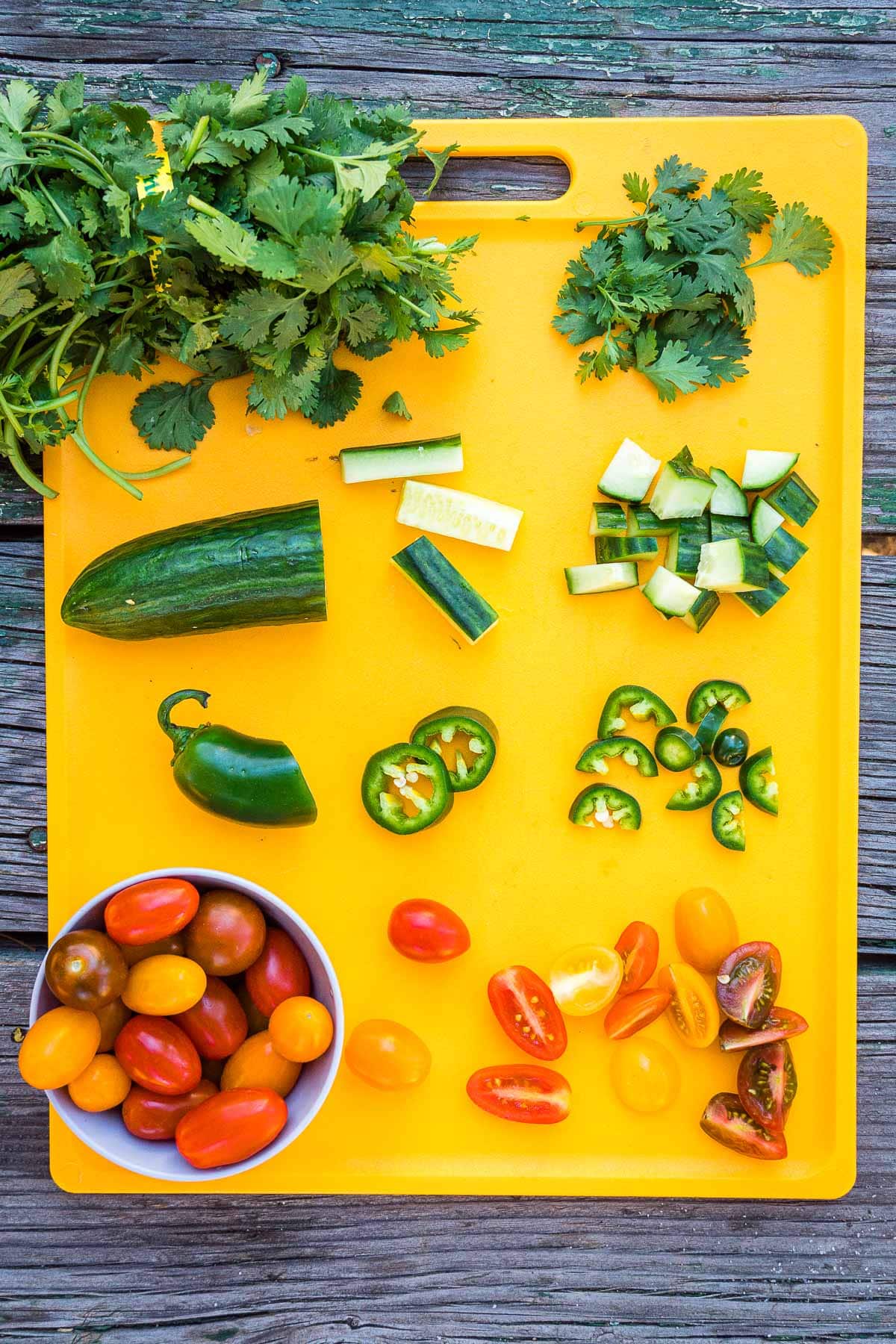 Herbs, cucumber, jalapeno and cherry tomatoes chopped on a cutting board