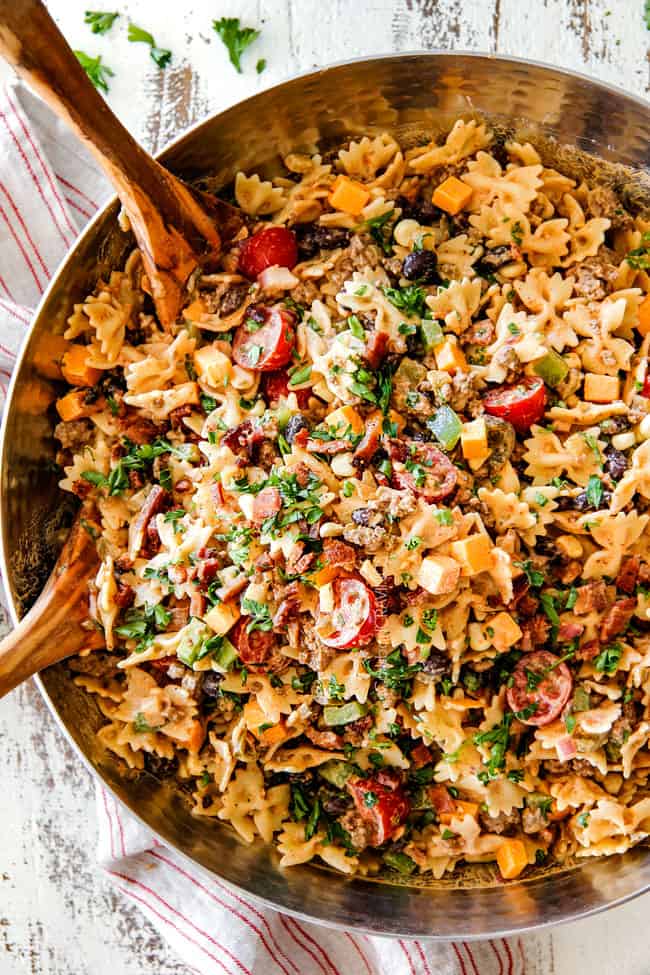 A pasta dish garnished with herbs, cherry tomatoes, ground meat, and olives, is placed on a rustic wooden table.