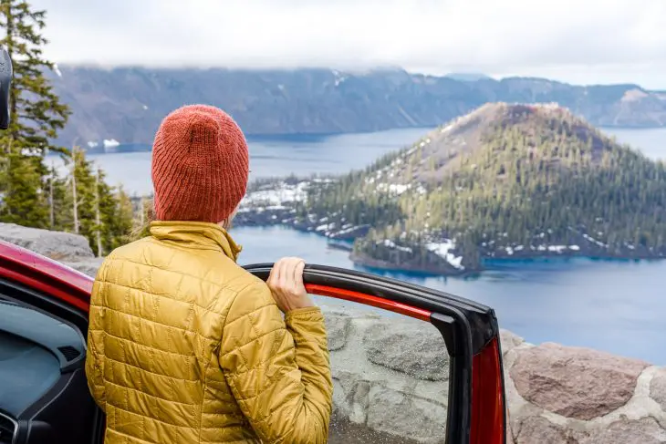 Megan stands next to a red car and looks out at Crater Lake