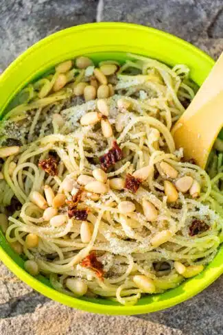 Pasta with pesto sauce, pine nuts, and sun dried tomatoes in a bowl.