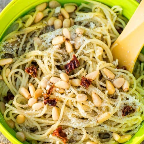 Pasta with pesto sauce, pine nuts, and sun dried tomatoes in a bowl.
