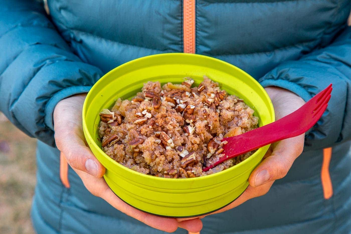 Megan holding a green backpacking bowl full of apple quinoa porridge