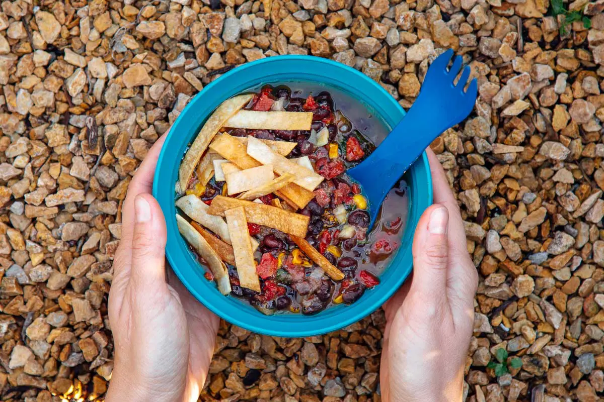 A bowl of tortilla soup on a natural background with hands