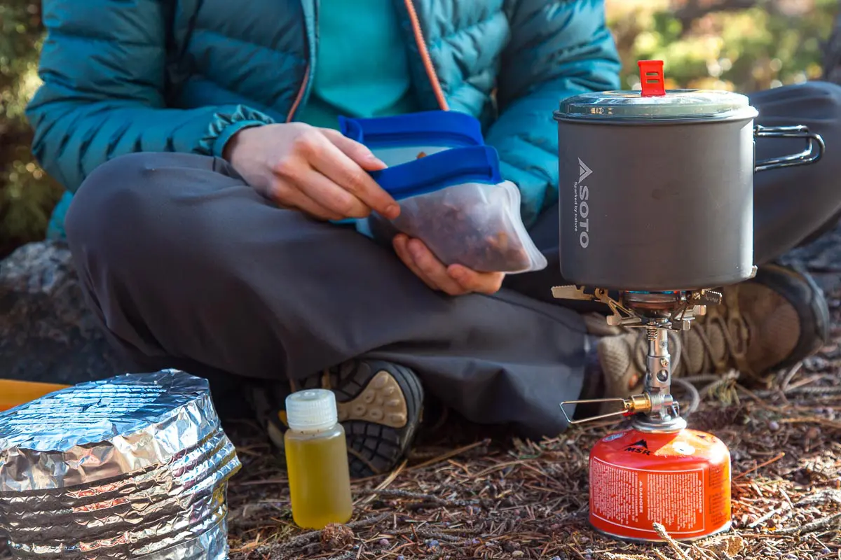 Megan holding a bag of backpacking food with a pot on a stove in the foreground