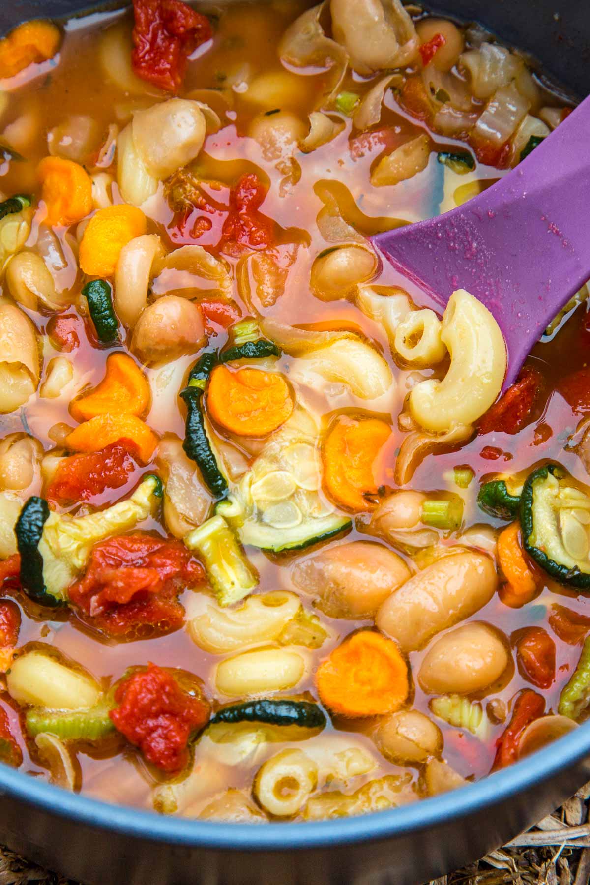 Minestrone soup in a pot with a purple spoon