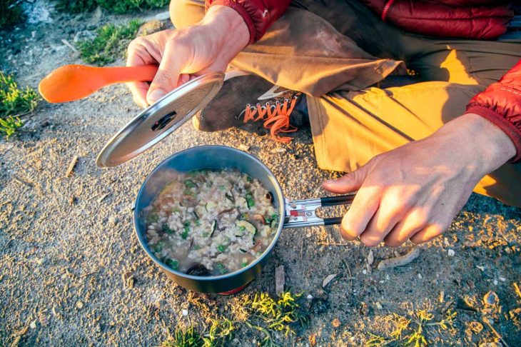 Dehydrated risotto in a backpacking pot. A man is lifting up the lid.