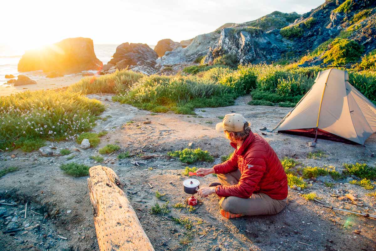 Michael sitting on the ground with a camp scene and sunset