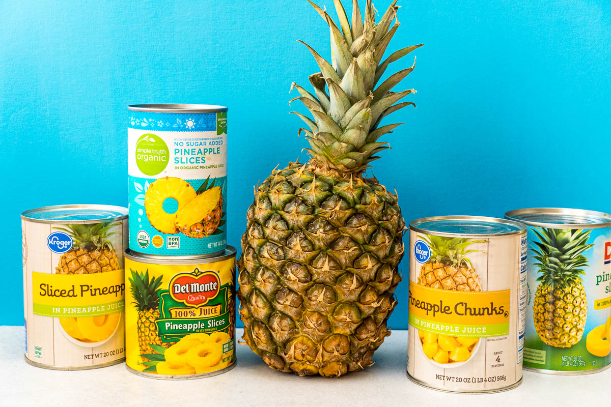 A whole pineapple next to several cans of pineapple