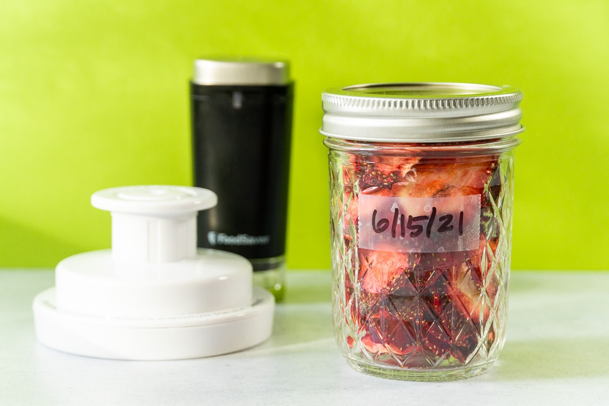 Dried strawberries in a jar with a handheld vacuum sealer in frame