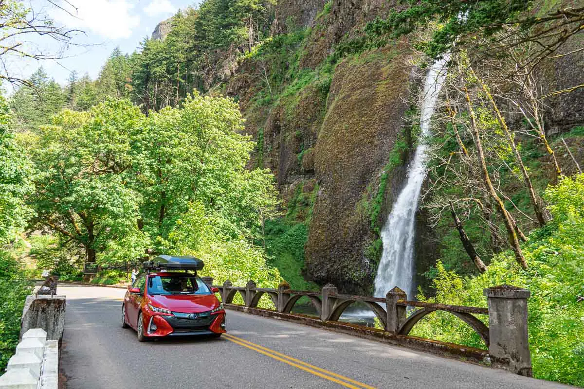 A red Prius Prime driving on a bridge next to a waterfall.