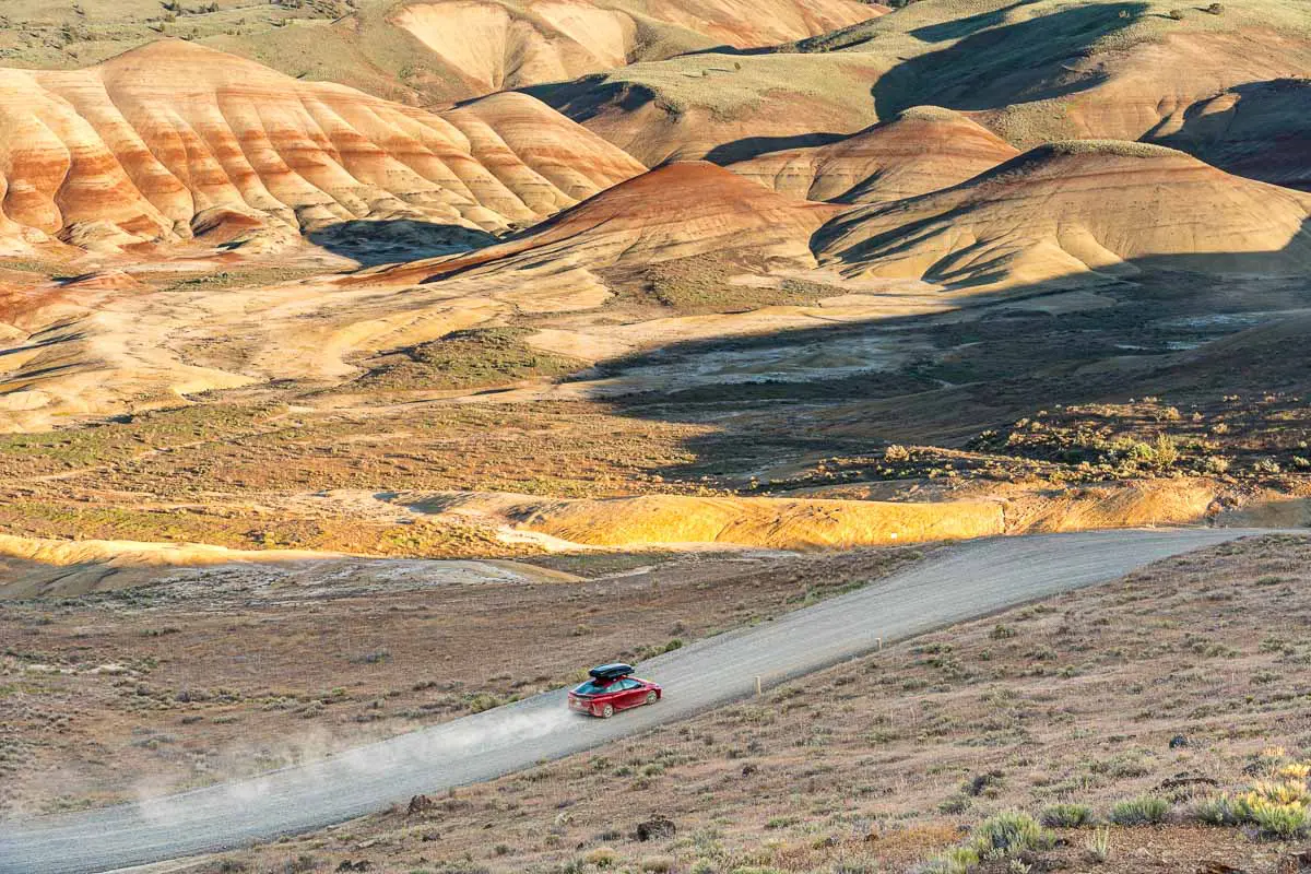 A red Prius Prime driving down a road towards the Painted Hills.