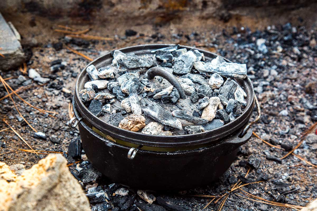 Dutch oven in a fire pit with embers on the lid