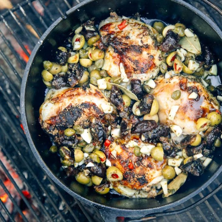 Chicken, green olives, and dried prunes in a Dutch oven in a fire pit