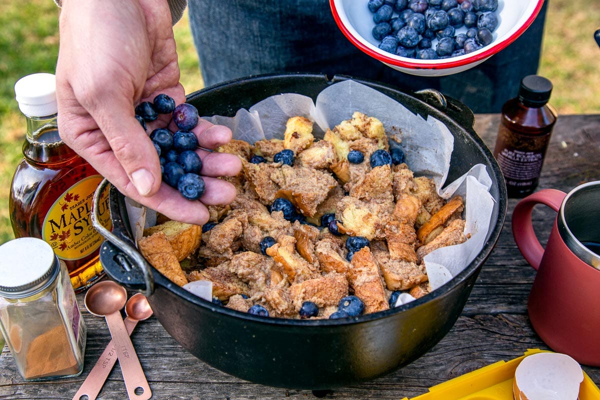 Michael's hand is full of blueberries and he is placing them in a Dutch oven that is filled with torn bread.