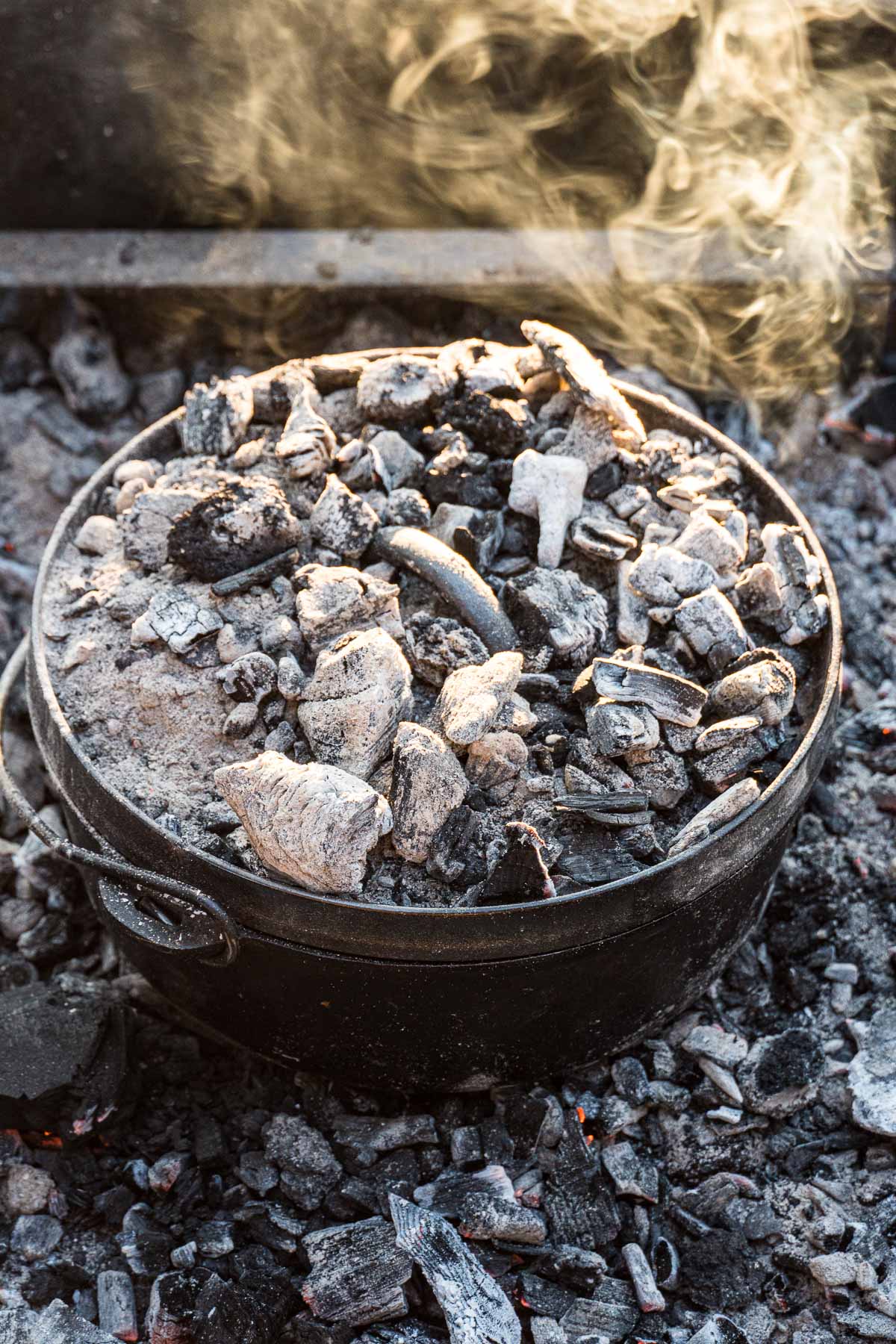 A Dutch oven in a campfire ring covered with coals.