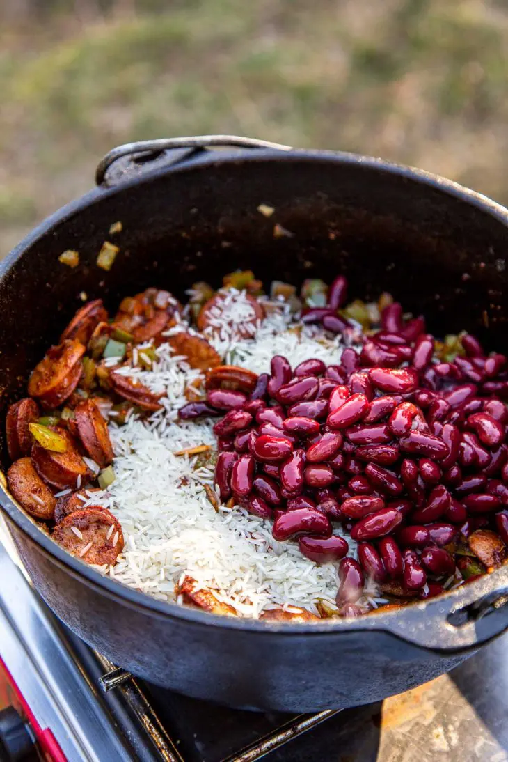 A dutch oven full of vegetables, beans, and rice sitting on a camp stove.