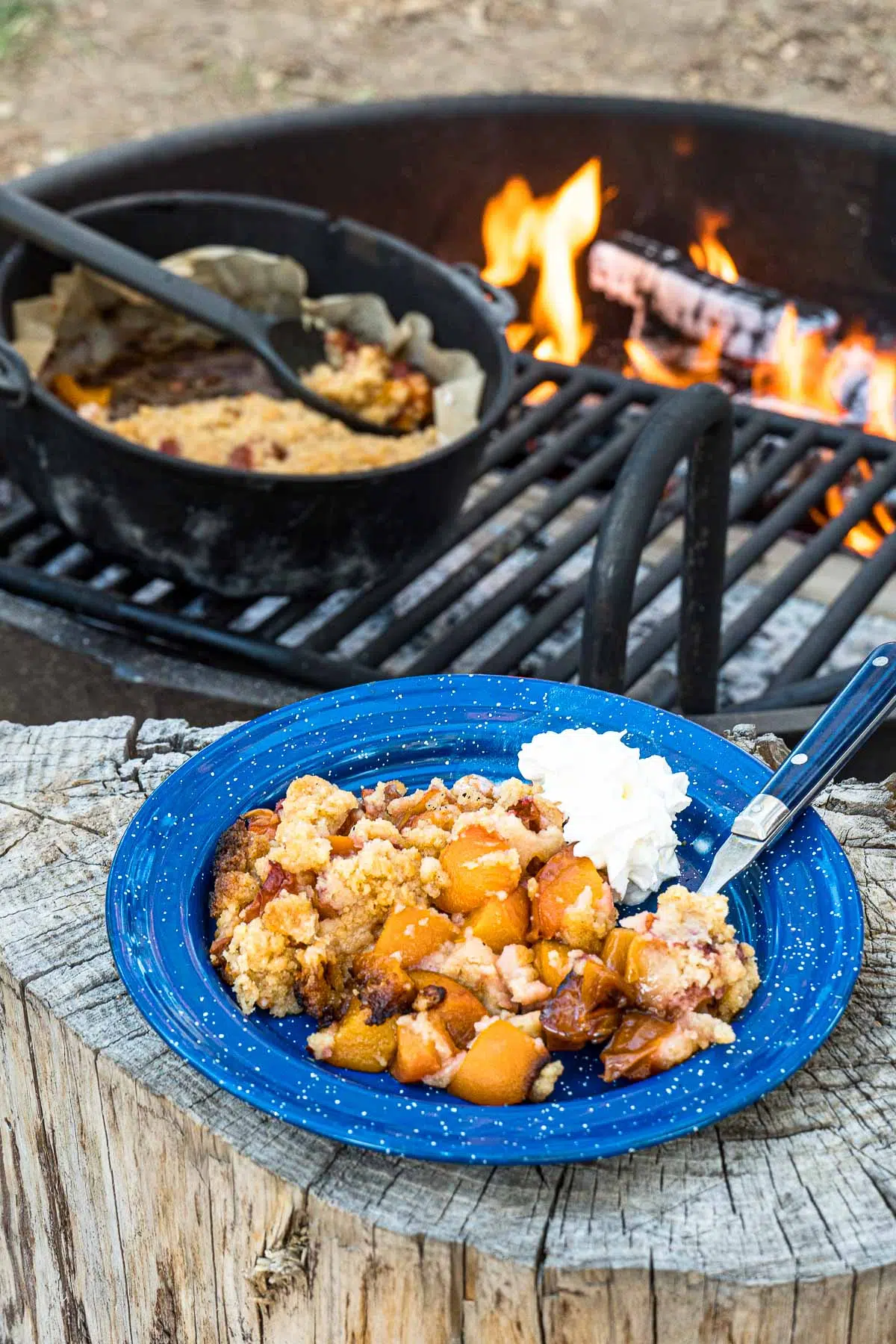 Peach cobbler on a plate with a campfire in the background