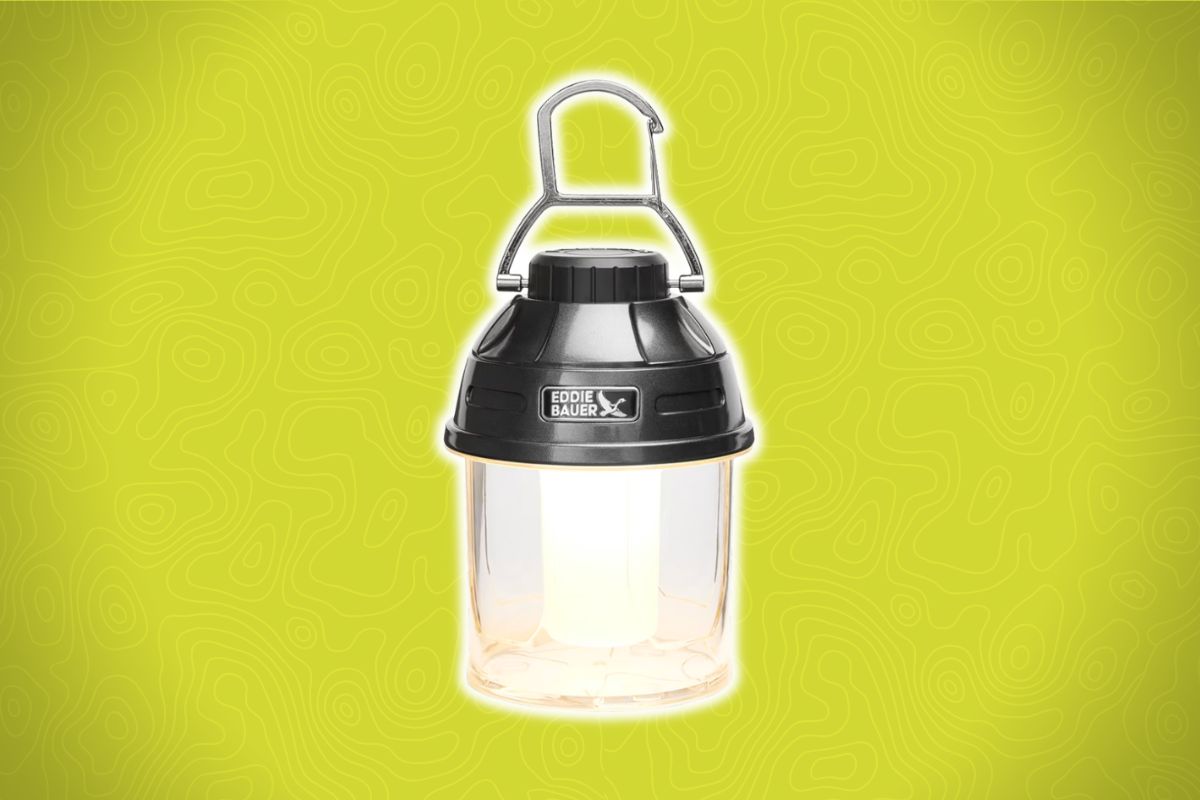 A black and silver Eddie Bauer lantern with a handle sits against a bright yellow background with faint topographic lines.