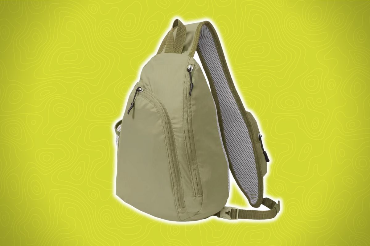 A khaki sling backpack with several zippered compartments and a padded, adjustable single strap sits on a yellow wavy-patterned background.