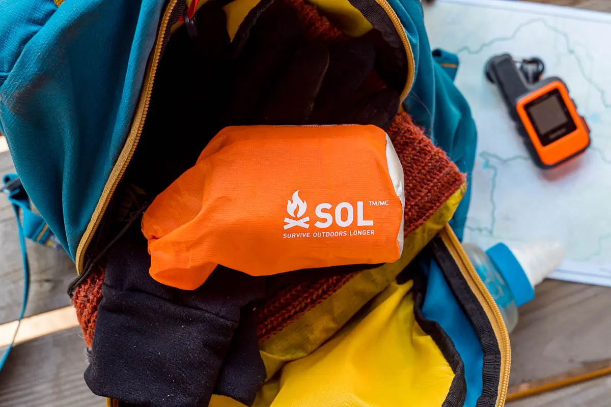 An orange bag containing an emergency bivy in a backpack