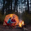 Megan and Michael sit near a campfire with a camping tent in the background