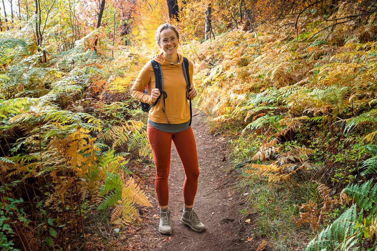 Megan standing in the middle of a trail that is lined with yellow and green ferns