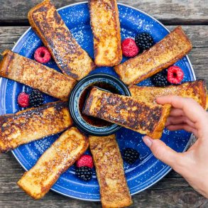 French Toast Sticks fanned out on a blue plate with a small bowl of syrup.