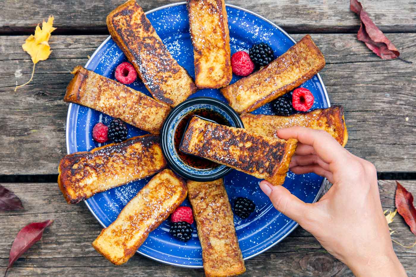 French Toast Sticks fanned out on a blue plate with a small bowl of syrup.