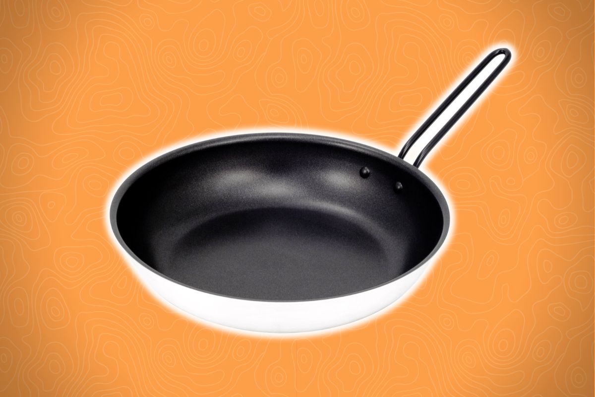 A nonstick frying pan with a metal handle sits on an orange background with a subtle wavy pattern.
