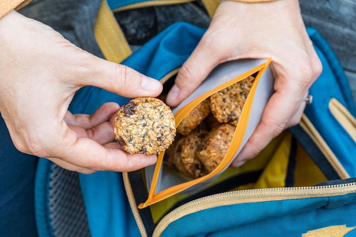 Megan holding a granola bite next to a blue hiking day pack