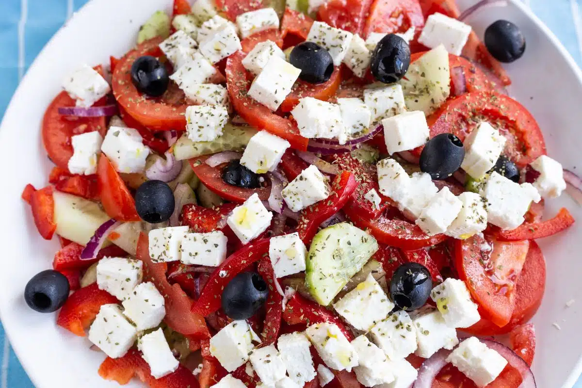 Chopped tomatoes, cucumbers, feta cheese, and olives in a white bowl.