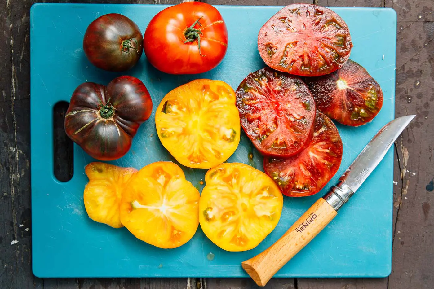 Red and yellow heirloom tomato slices on a blue cutting board