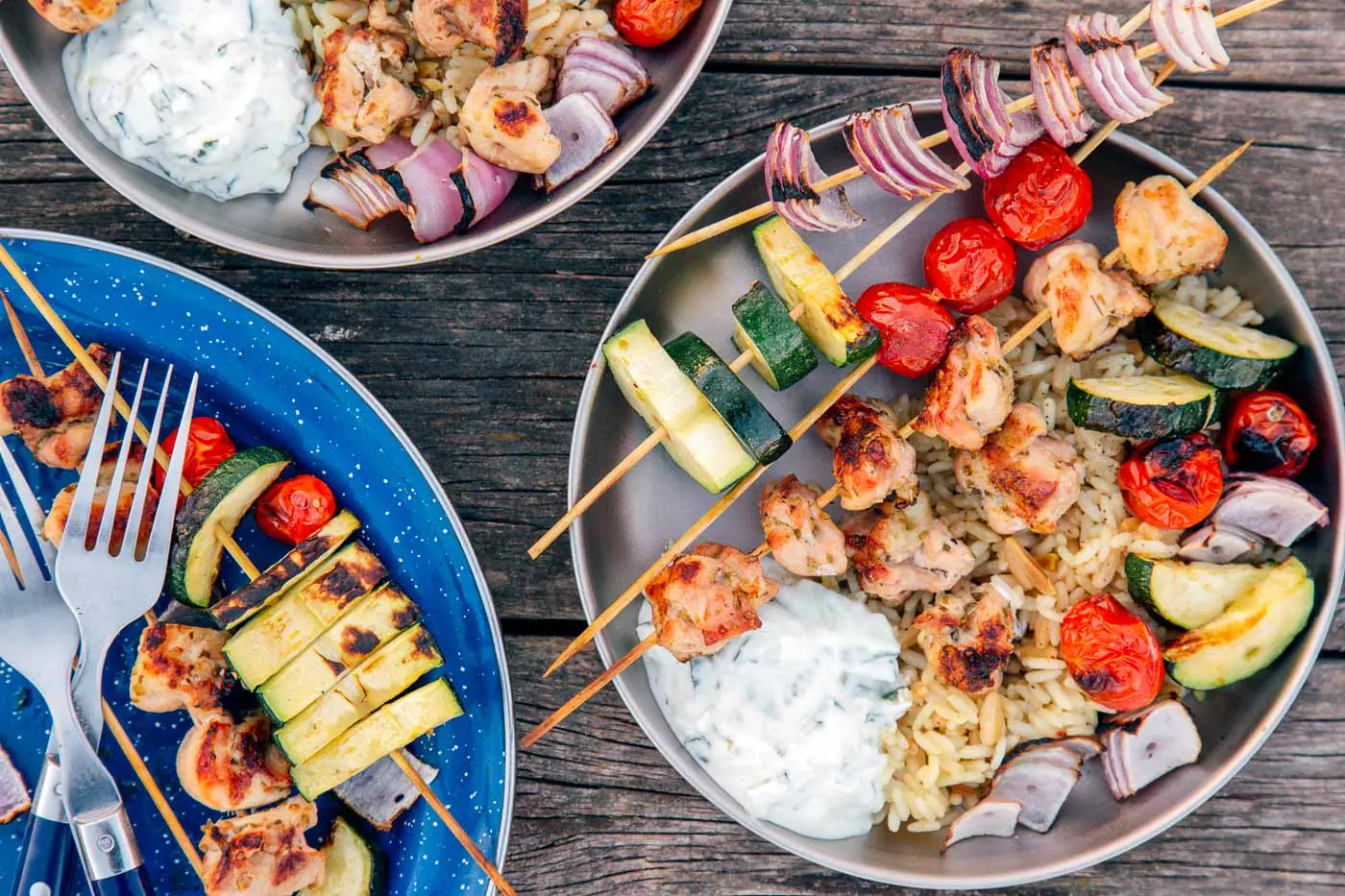 Grilled chicken kabobs on blue and silver camping plates.